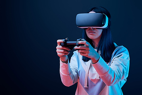 KYIV, UKRAINE - APRIL 5, 2019: Selective focus of brunette woman playing video game while wearing virtual reality headset on blue