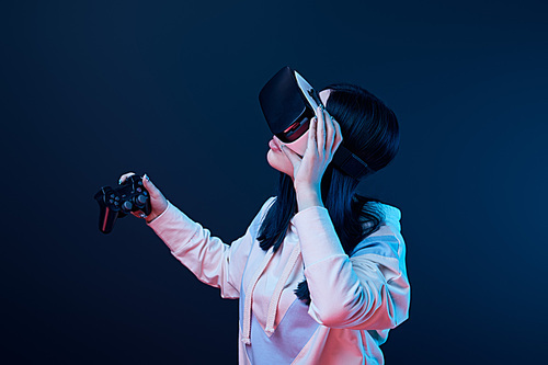 KYIV, UKRAINE - APRIL 5, 2019: Brunette woman holding joystick while touching virtual reality headset on blue