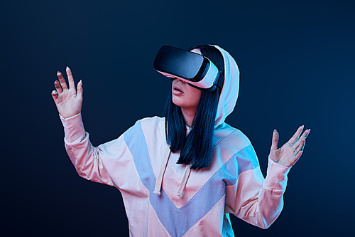 surprised brunette woman gesturing while using virtual reality headset on blue