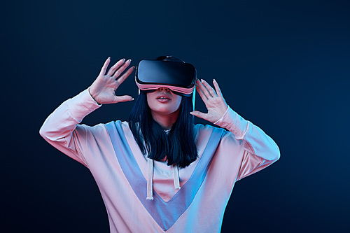 surprised young woman gesturing while using virtual reality headset on blue
