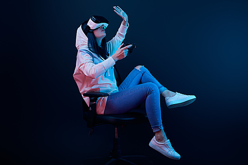 KYIV, UKRAINE - APRIL 5, 2019: Brunette woman holding joystick and gesturing while wearing virtual reality headset on blue