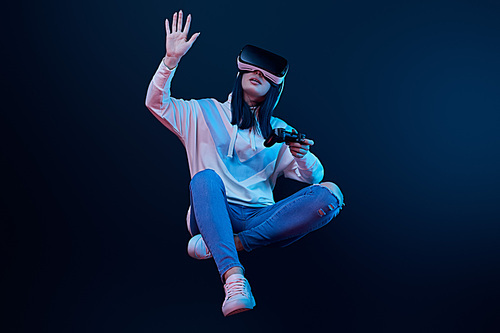 KYIV, UKRAINE - APRIL 5, 2019: Woman holding joystick and levitating while gesturing and wearing virtual reality headset on blue