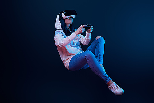 KYIV, UKRAINE - APRIL 5, 2019: Young woman in virtual reality headset levitating and holding joystick on blue