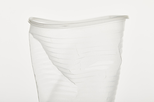 close up view of crumpled transparent plastic cup on white background