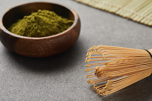 selective focus of bamboo whisk and green matcha powder in wooden bowl