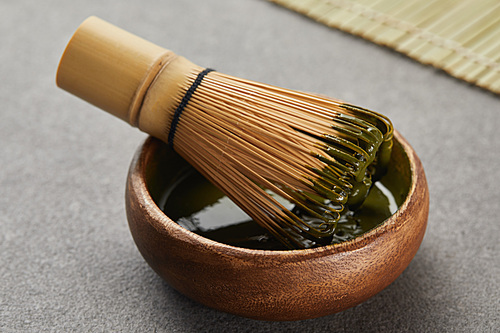 selective focus of bamboo whisk in wooden bowl with green matcha powder