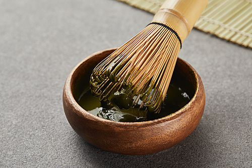 selective focus of bamboo whisk in wooden bowl with green matcha powder