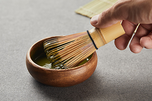 selective focus of man holding bamboo whisk in wooden bowl with green matcha