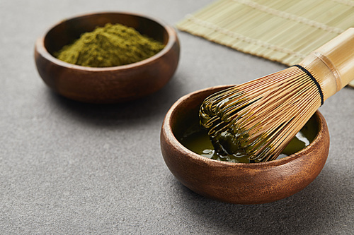 selective focus of matcha powder bowl near bamboo whisk in green tea