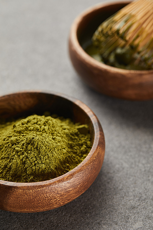 selective focus of green matcha powder and bamboo whisk in wooden bowl