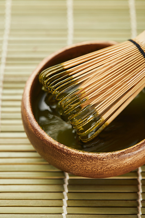 selective focus of green matcha powder and bamboo whisk in wooden bowl on table mat