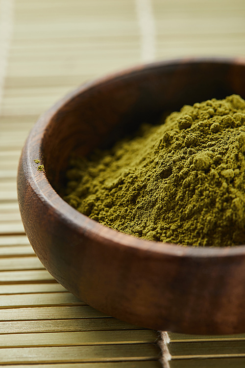 selective focus of green matcha powder in wooden bowl on table mat