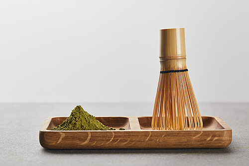 green matcha powder and bamboo whisk on wooden board
