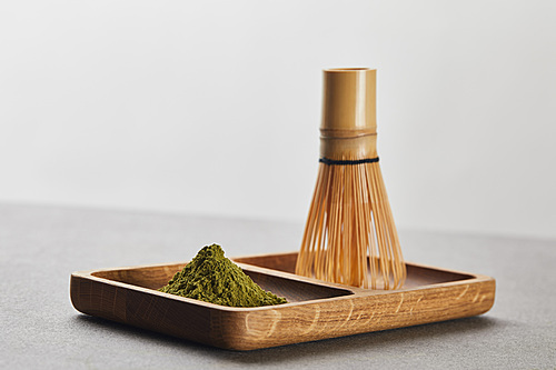 selective focus of green matcha powder and bamboo whisk on wooden board
