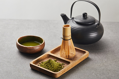 selective focus of green matcha powder and bamboo whisk on wooden board near 홍차pot and bowl with tea