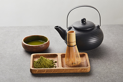green matcha powder and bamboo whisk on wooden board near 홍차pot and bowl with tea