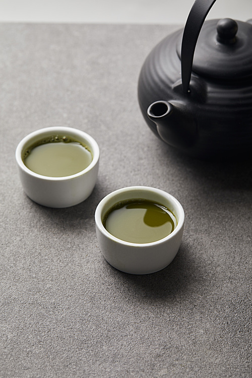 selective focus of 홍차pot and white cups with matcha tea on grey stone table