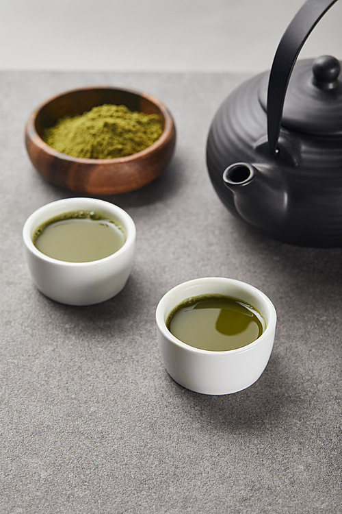 selective focus of green matcha powder in wooden bowl near cups with tea and 홍차pot