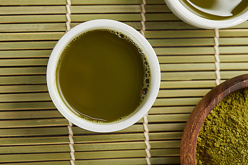 top view of white cups with green tea near matcha powder in wooden bowl