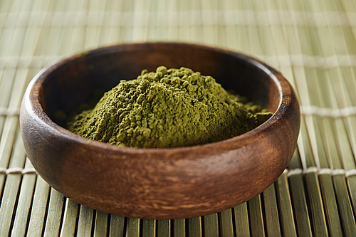 selective focus of green matcha powder in wooden bowl on bamboo table mat