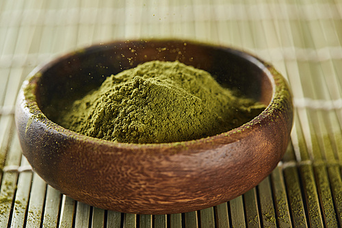 selective focus of green matcha powder in wooden bowl on bamboo table mat