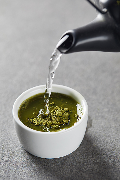 black kettle pouring water in white cup with green matcha powder