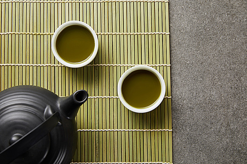 top view of white cups with green matcha tea near 홍차pot on bamboo table mat