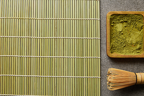 top view of green matcha powder on wooden board near bamboo whisk and table mat
