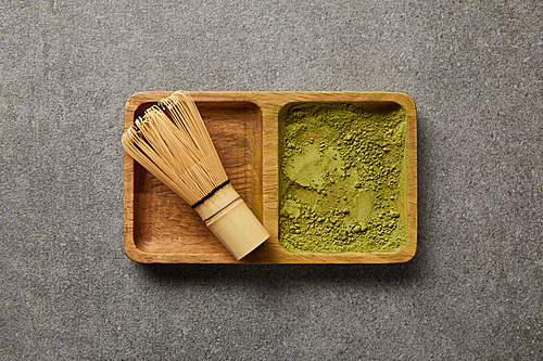 top view of bamboo whisk with matcha powder in wooden bowl on grey table