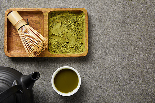 top view of bamboo whisk and matcha powder on board near 홍차pot and white cup with green tea