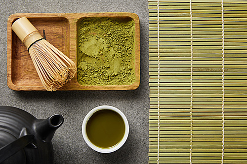 top view of bamboo whisk with matcha powder in wooden bowl near white cup, 홍차pot and table mat