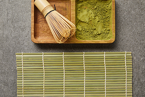 top view of bamboo whisk and green matcha powder on board near table mat