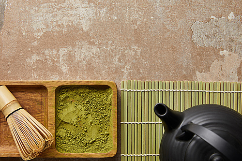top view of matcha powder and bamboo whisk on board near 홍차pot on aged surface