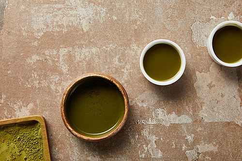 top view of matcha powder, bowl and cups with green tea on aged surface