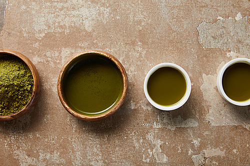 top view of matcha powder, bowl and cups with green tea on aged surface