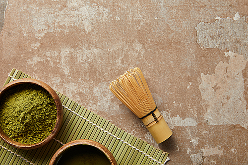 top view of matcha powder in wooden bowl near green tea and bamboo whisk
