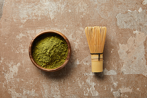 top view of matcha powder in wooden bowl with bamboo whisk on aged surface