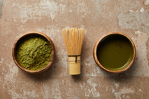 top view of matcha tea and powder in wooden bowl with bamboo whisk on aged surface