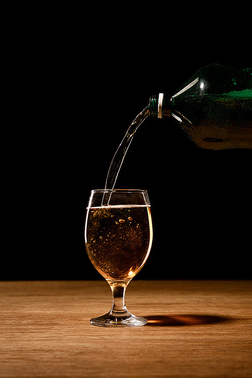 beer pouring from bottle in glass on wooden table isolated on black