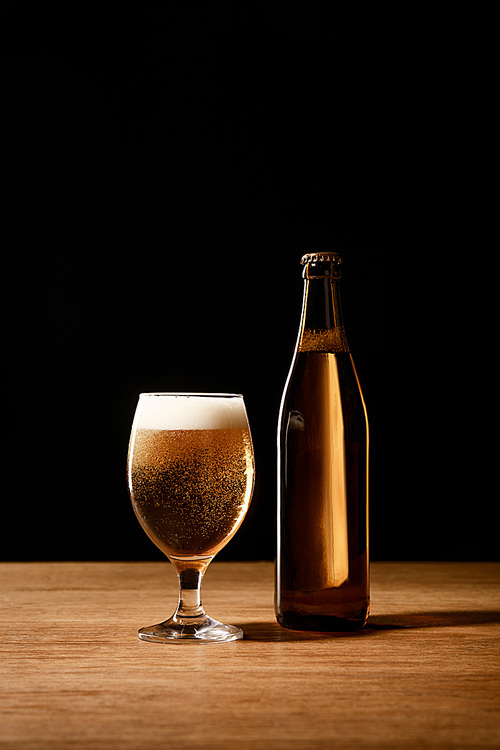 beer in glass with foam and in bottle on wooden table isolated on black