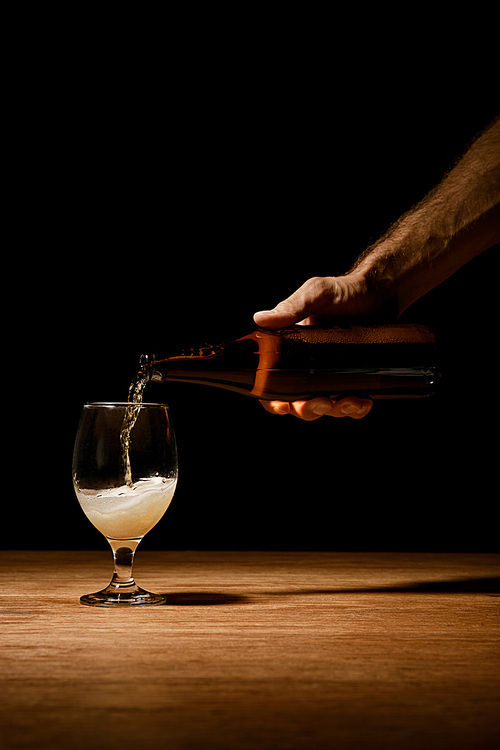 cropped view of man pouring beer from bottle in glass on wooden table isolated on black