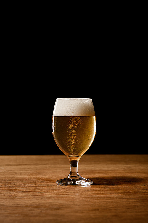 glass of beer with white foam on wooden table isolated on black