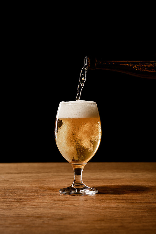 beer pouring from bottle in glass isolated on black