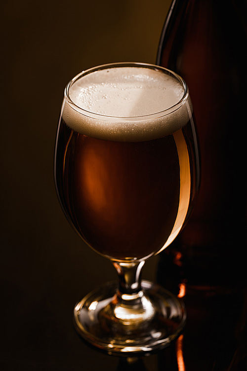 close up view of beer with white foam in glass on dark background with lighting