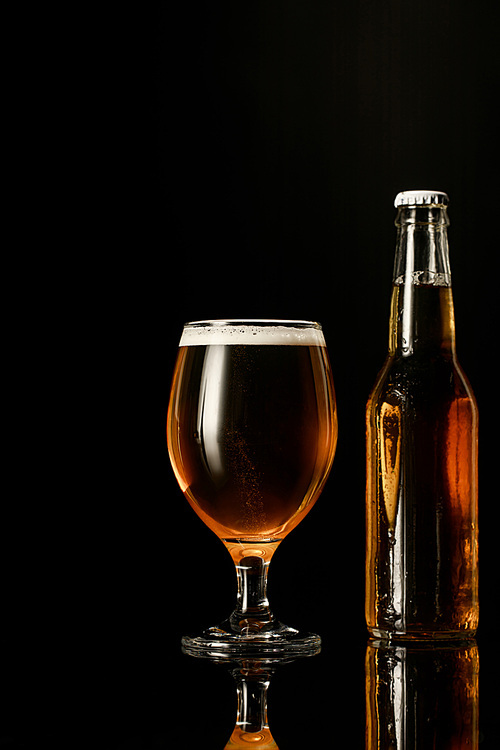 glass of beer with foam near bottle isolated on black