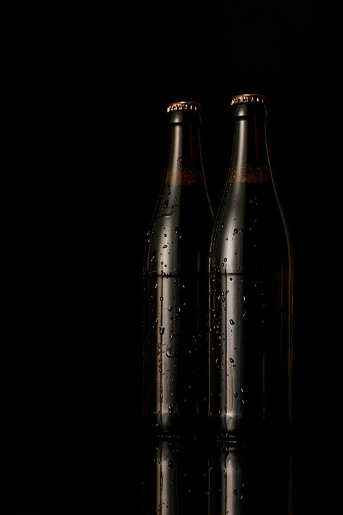 glass bottles of beer with drops isolated on black
