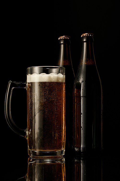 glass of beer with foam near wet bottles isolated on black