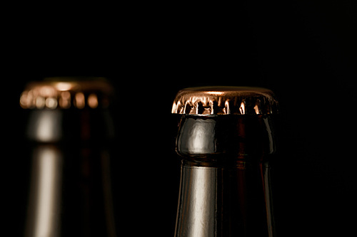 close up view of glass bottles of beer with metal caps isolated on black