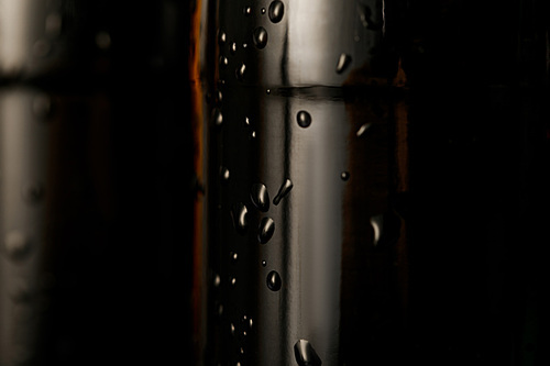 close up view of glass bottle of beer with water drops isolated on black