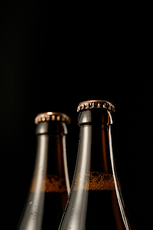 close up view of glass bottles of beer with caps isolated on black